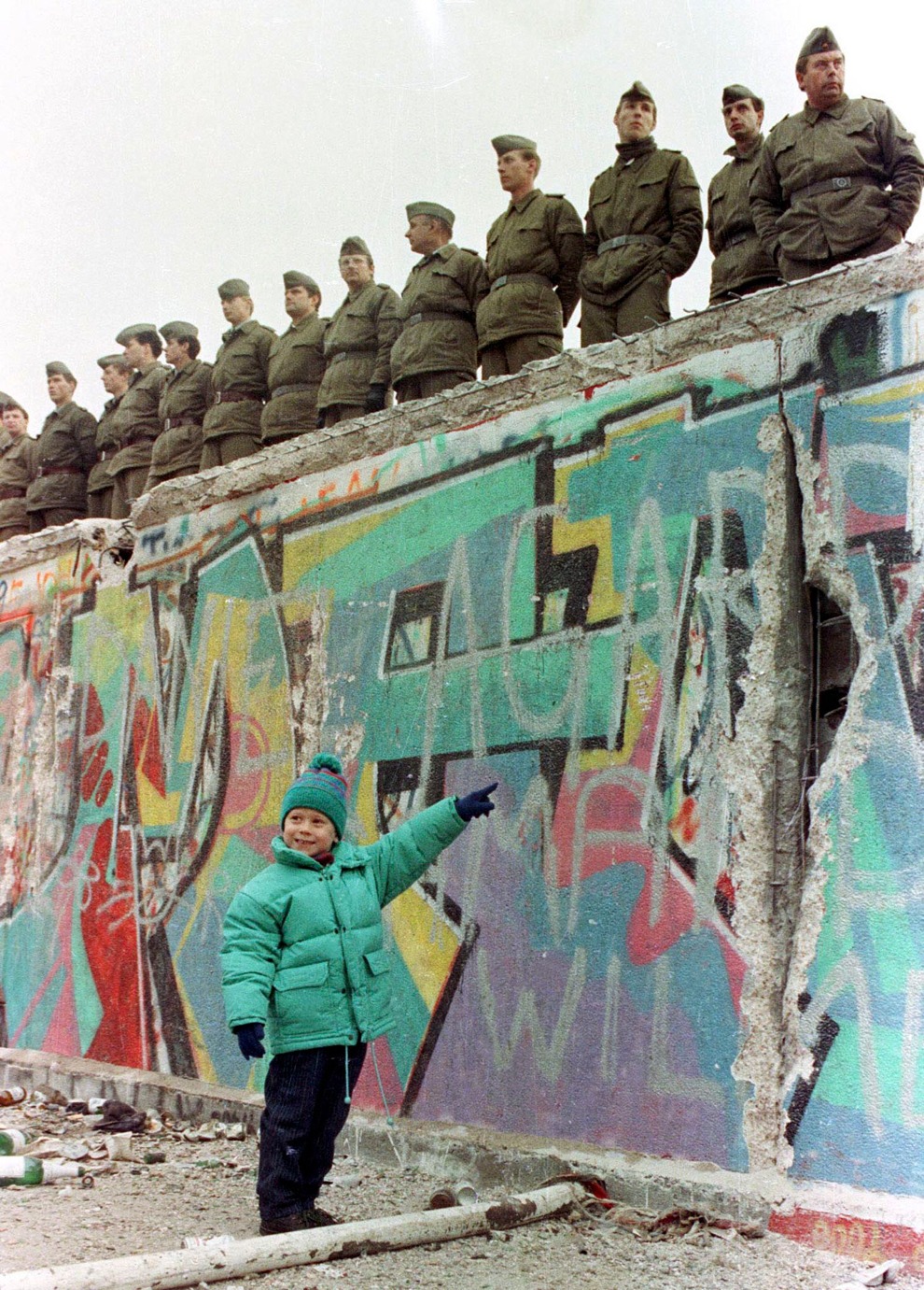 Западногерманская девочка показывает на дыру в стене. Сверху за этим всё ещё наблюдают восточногерманские солдаты