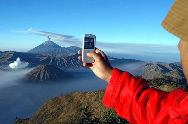 Туристы используют свой мобильный телефон, чтобы сфотографировать извержение вулкана в  Индонезии