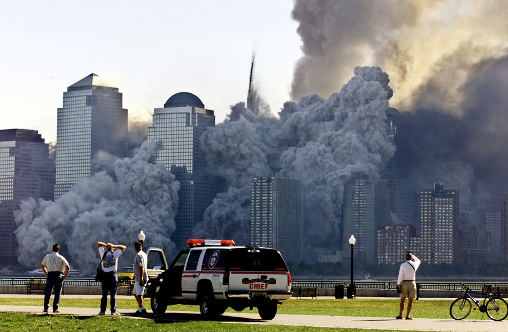 Люди смотрят издали на облако пыли и мусора, которое взметнулось после падения башен Всемирного торгового центра
