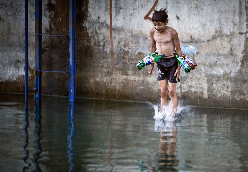  Мальчик прыгает в реку с пустые пластиковые бутылки вокруг его талии для  равновесия, в Бухаресте, Румыния, в жаркий день