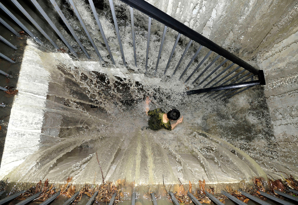 Житель пробегает по затопленной лестнице,  вода вливается в подземный гараж. Проливные дожди в Чэнду, провинция Сычуань, Китай,