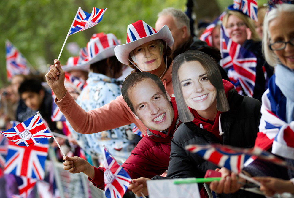 Поклонники размахивают британскими  флажками и надевают маски с изображениями королевской четы