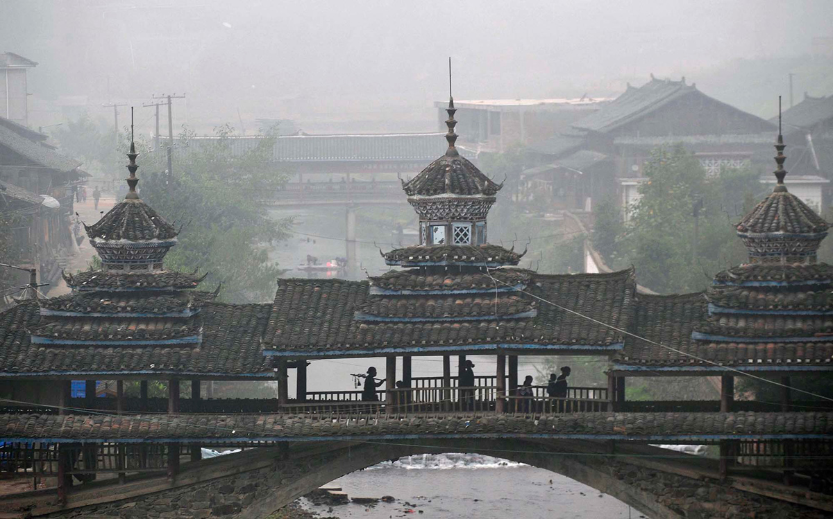 Жители народности дун проходят через крытый мост, на пути к Большому хору Кам, в деревне Тунгуань, Липинского уезда.