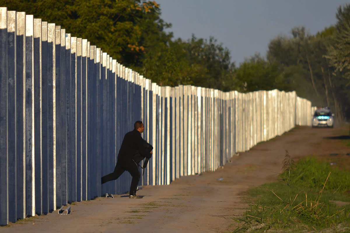 Мигрант бежит, прорвавшись на территорию Венгрии, преодолев забор временной защиты, установленный вдоль венгерско-сербской границы, в момент, когда к нему приближается полицейская машина, Реске (Rоszke), Венгрия, 7 сентября 2015 года.
