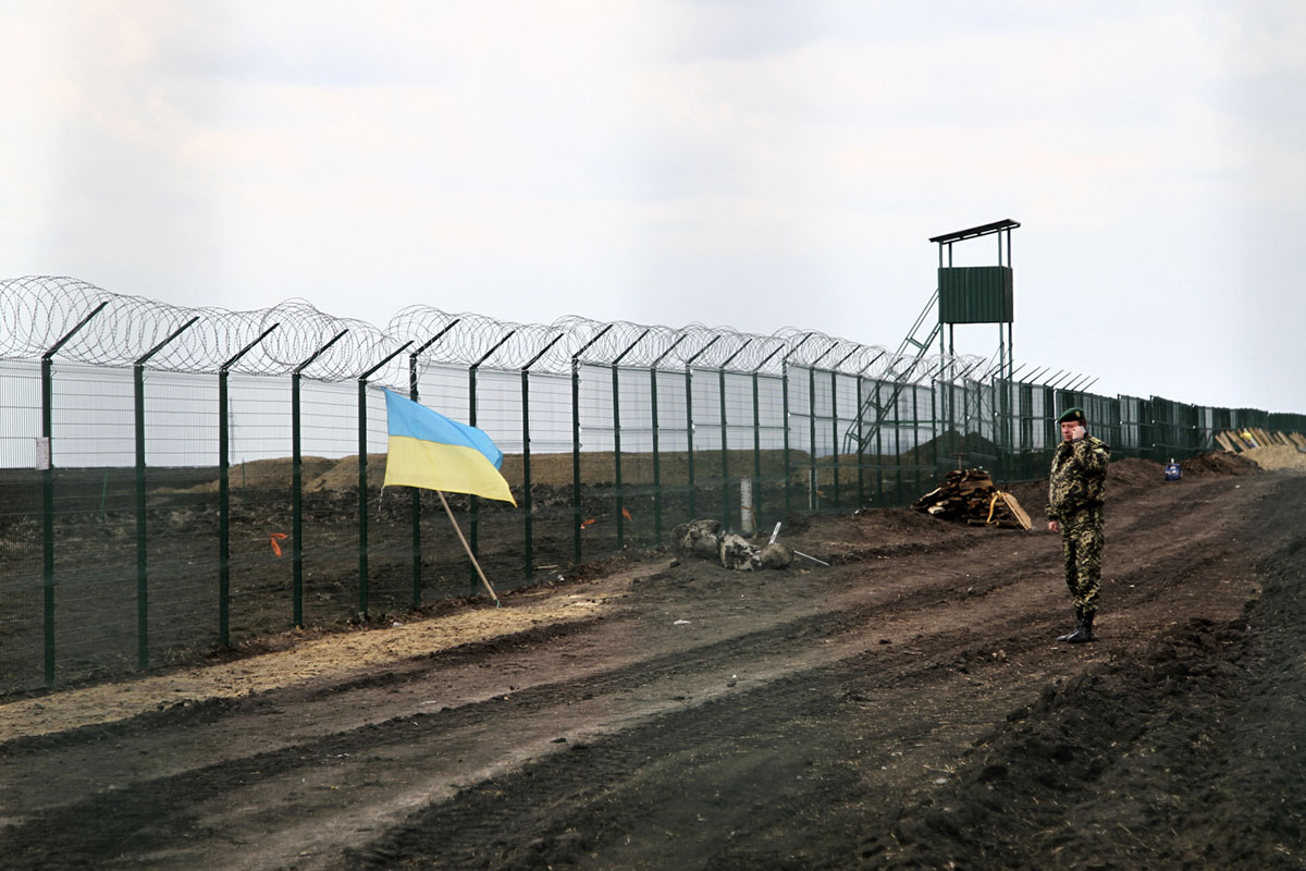 Украинский пограничник говорит по телефону рядом с национальным флагом, прикрепленным к забору на украинско-российской границе возле Гоптовки, Харьковская область, Восточная Украина, 18 апреля 2015 года.
