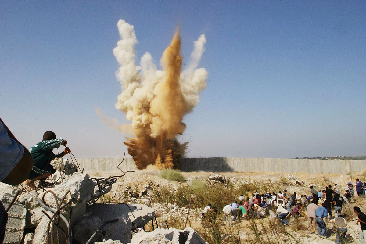 Палестинский мальчик сидит на бетонном выступе, наблюдая за тем, как возле толпы людей, желающих пересечь границу с Египтом, взорвалась стена, разделяющая город Рафах (Rafah), расположенный на юге Сектора Газа, и Египет, 14 сентября 2005 года. По словам очевидцев, боевики ХАМАС проделали зияющую дыру в бетонном заграждении, которое было поспешно возведено, чтобы остановить палестинцев, хлынувших через Сектор Газа в Египет. В течение ночи на границе Рафах было установлено несколько гигантских бетонных блоков, таким образом египетские и палестинские должностные лица попытались положить конец хаосу.
