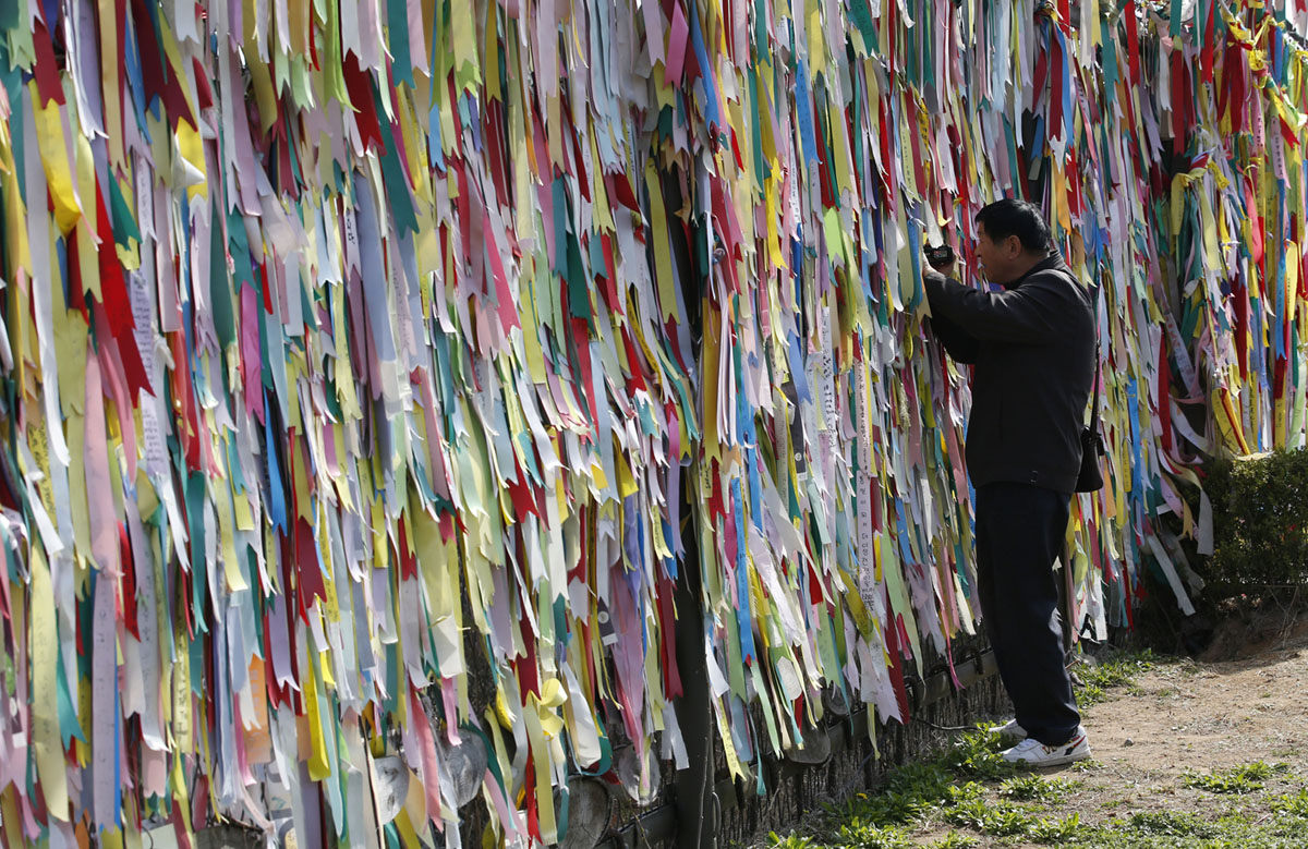 Мужчина снимает видео через забор, украшенный лентами, на которых посетители оставили пожелания о воссоединении двух Корей в павильоне Имджингак (Imjingak) недалеко от границы с Северной Кореей, Паджу (Paju), Южная Корея, 15 апреля 2016 года.