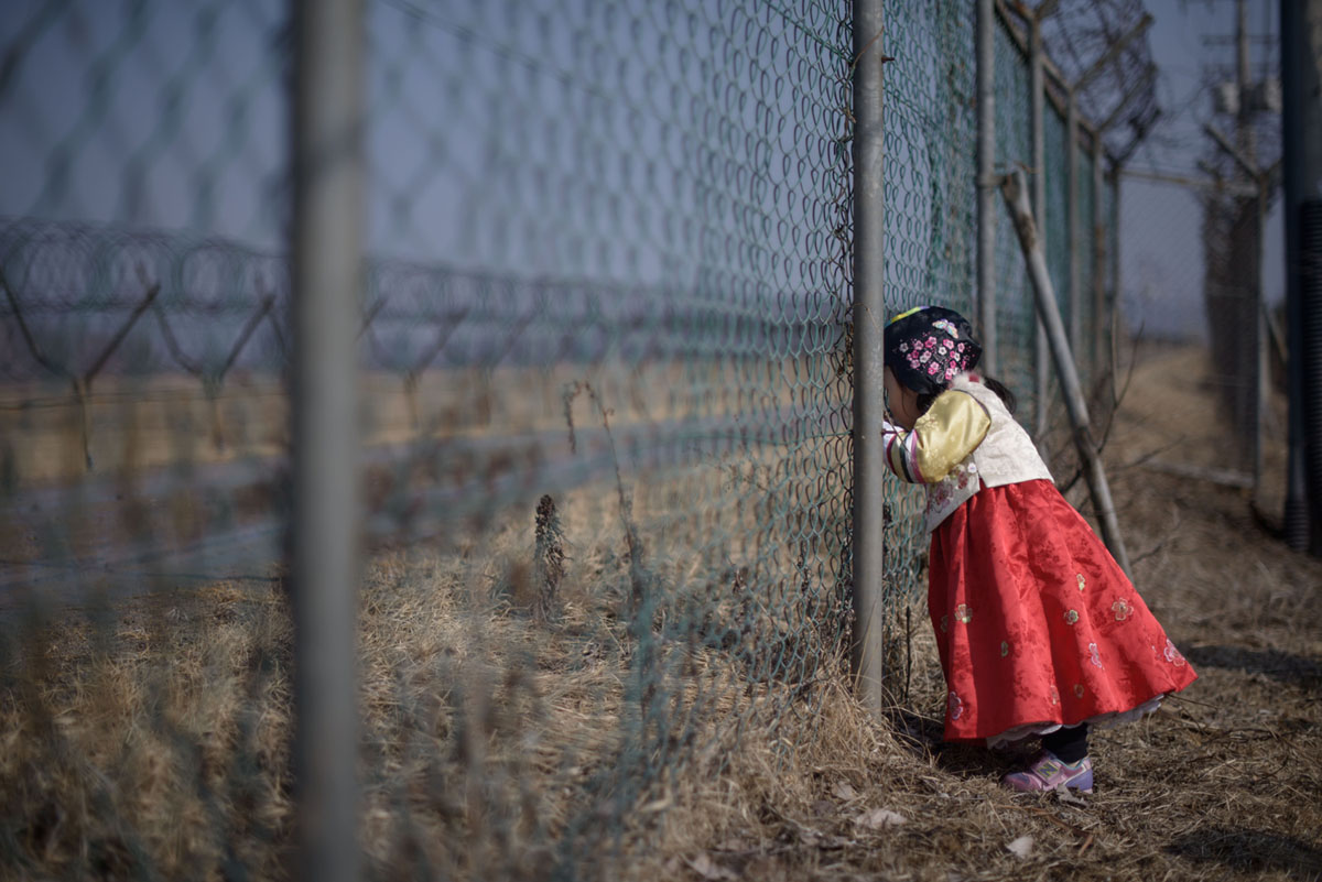 Девочка в традиционном корейском платье ханбок смотрит через военный забор в сторону Северной Кореи в парке Имджингак (Imjingak), расположенном к югу от военной демаркационной линии и демилитаризованной зоны (ДМЗ), разделяющей Северную и Южную Корею, 19 февраля 2015 года. Многие южнокорейские семьи, разлученные во время Корейской войны, посещают ДМЗ, чтобы вознести молитвы за своих родственников, живущих в Северной Корее, по случаю Лунного Нового года.